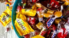 a blue bowl filled with assorted candy on top of a wooden table next to other candies