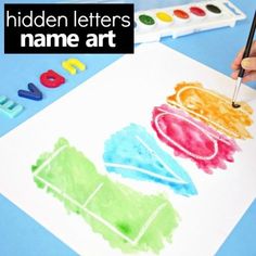 a child's hand holding a paintbrush and drawing on paper with the words hidden letters name art