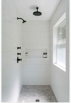 a white tiled bathroom with black and white tile on the shower head, window, and faucet