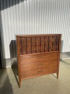 a wooden dresser sitting in front of a white building with a metal wall behind it