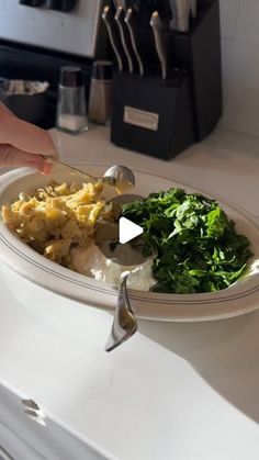 a person holding a spoon over a plate of food on a counter top next to a knife and fork