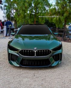 the front end of a green sports car parked on top of a gravel lot next to trees