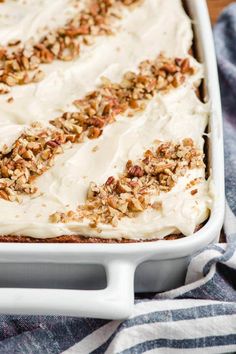 carrot cake with cream cheese frosting and pecans on top in a white dish