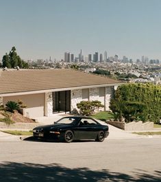 a black car parked in front of a house with a view of the city behind it