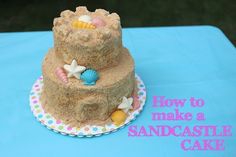 a sandcastle cake with shells and seashells on it, sitting on a blue table cloth