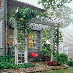 a house that has some plants growing on the front and side of it with red pillows