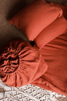 an orange pillow and some red pillows on a bed