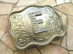 This stunning silver tone belt buckle features a rhinestone covered letter E initial, on an etched belt buckle lightly embellished with rhinestones.The buckle is bright silver in color with a rope border.The buckle measures 3 1/2 x 2 3/4 and has a hook and D ring loop that attaches to any 1.5" width belt strap. As with any internet purchase, I recommend using these measurements against a buckle you already own.All Step Originals belt buckles have my hand etched signature.This is Truly a One-Of-A Sparkly Belts, Initial E, Rhinestone Belt Buckle, H Monogram, Cowgirl Belts, Kids Belt, Western Buckles, Silver Belt Buckle, Western Belt Buckles