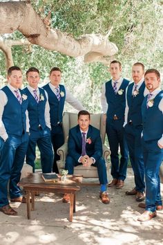 a group of men standing and sitting next to each other in front of a tree