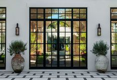 two large vases with plants are in front of the entrance to a building that has glass doors