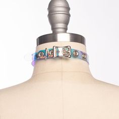 Classic choker collar in iridescent, holographic vinyl layered over PVC. An aurora borealis chandelier crystal point adorns the center o-ring. Fit is adjustable with buckle. Holes are reinforced with grommets.This is the mini version - slightly slimmer with a smaller crystal for a more delicate look!Collar is 1/2" wide, with a 1" crystal point.SMALL/MEDIUM (11-13")MEDIUM/LARGE (13-15")LARGE/X-LARGE (15-17")Custom sizing available.  All pieces are MADE TO ORDER, standard sizes S/M-L/XL.  If your Adjustable Iridescent Choker Jewelry, Adjustable Rave Choker For Festival, Adjustable Multicolor Rave Choker, Adjustable Rave Style Choker, Rave Multicolor Choker For Festivals, Rave Style Multicolor Choker, Pink Choker, Harness Bra, Bullet Bra