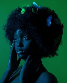 a woman with an afro and flowers on her head poses for a photo in front of a green background