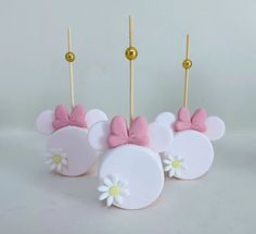 three cake pops with minnie mouse ears and daisies on them, sitting next to each other