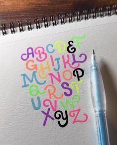 a pen is sitting on top of a notebook with the letters drawn in different colors