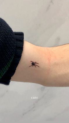 a small spider tattoo on the left inner arm and wrist is shown in black ink