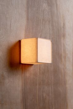 a wooden wall mounted light with a square shade on it's left side, against a wood paneled background