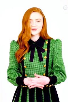 a woman with long red hair wearing a green and black dress standing in front of a white background