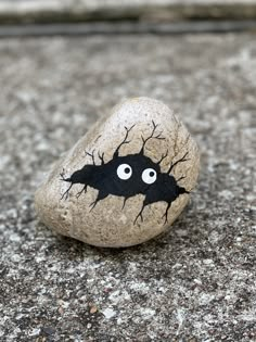 a rock with a black bat painted on it sitting on the ground next to a sidewalk