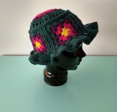 a crocheted hat with flowers on it sitting on a head mannequin