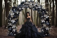 a woman wearing a black dress standing in front of a floral arch