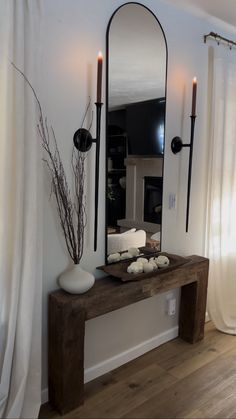 a mirror and some candles on a table in front of a fire place with white curtains