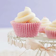 three cupcakes sitting on a wire rack with pink ribbons and bows around them