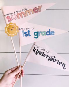 someone is holding up some paper flags with the words summer and first grade on them