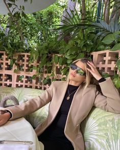 a woman sitting on top of a green couch next to a plant filled wall with potted plants