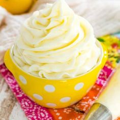 a yellow bowl filled with whipped cream on top of a colorful cloth next to two lemons