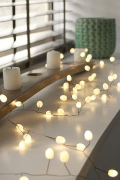 a bed with white lights on it next to a night stand and window sill