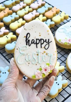 a person holding up a decorated cookie with the words happy easter on it in front of other decorated cookies