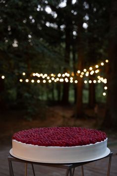 a white cake with red frosting sitting on top of a metal stand in front of some trees