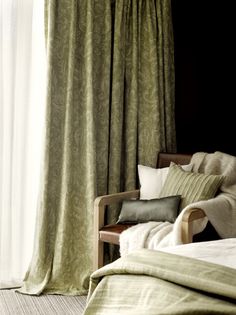 a bed sitting next to a window covered in green curtained drapes and pillows