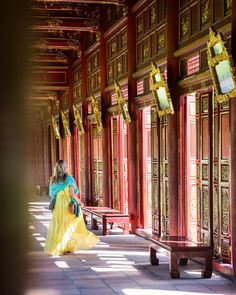 a woman in a long yellow dress is walking through an ornate building with red pillars