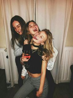 three girls are laughing and holding wine glasses in front of the camera while standing next to each other