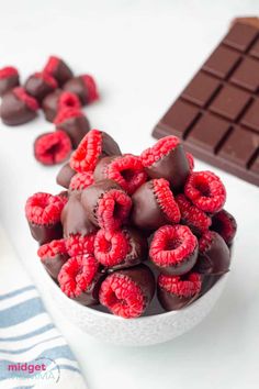 a bowl filled with raspberries next to some chocolates on a table top