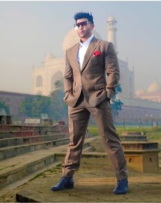 a man in a brown suit and sunglasses posing for a photo with the tajwa mosque in the background