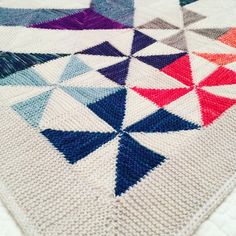 a multicolored crocheted blanket on top of a white tablecloth with blue, red, and purple triangles