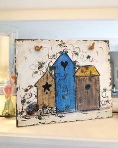 a painted sign with two birdhouses and a heart on it's side that says welcome