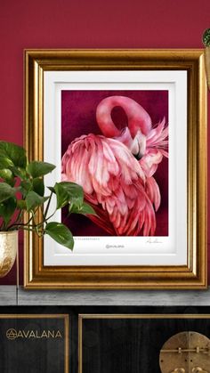 a pink flamingo in a gold frame sitting on a shelf next to a potted plant