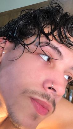 a close up of a man with curly hair and piercings on his nose looking off to the side