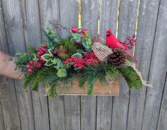 a wooden box filled with pine cones, berries and evergreens next to a fence