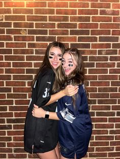 two girls are hugging each other in front of a brick wall and wearing face paint