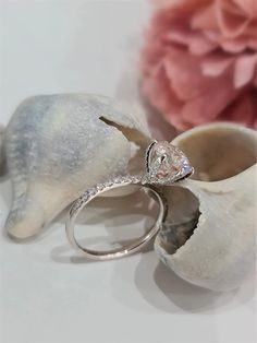 a diamond ring sitting on top of a seashell next to a pink flower and shell