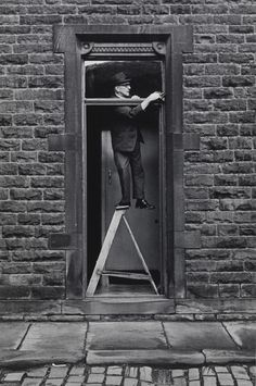 a man standing on a stepladder in front of a brick building with an open door