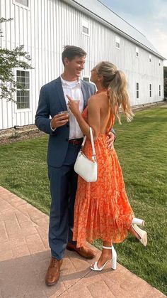 a man in a suit and tie standing next to a woman wearing an orange dress