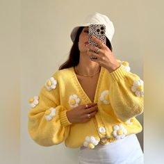 a woman taking a selfie while wearing a yellow sweater with flowers on the sleeves