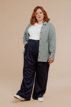 a woman standing with her hands in her pockets and looking at the camera while wearing wide pants