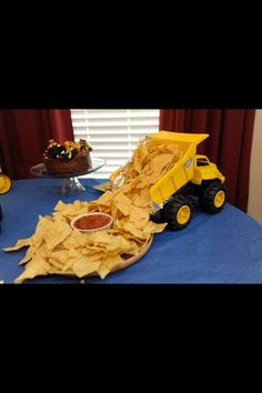 a table topped with lots of chips and a yellow truck next to it on top of a blue blanket