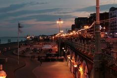 the boardwalk is lit up at night with people walking on it and buildings in the background